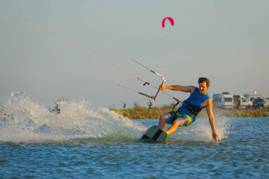 Cool male kitesurfer drags his hand along the calm surface of the blue ocean.