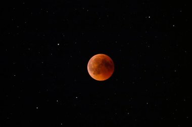 Spectacular close up view of a full moon glowing orange in the black night sky.
