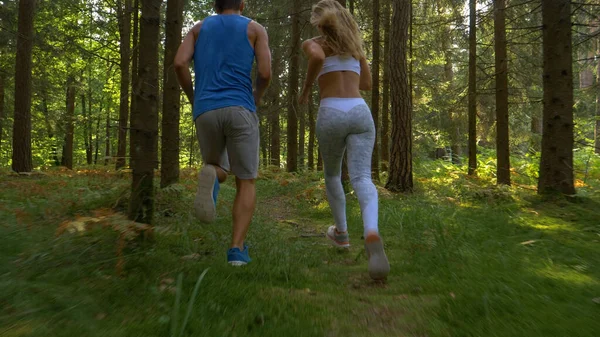 NAGY ANGLE: atlétikai férfi és sportos nő fut együtt az erdőben. — Stock Fotó