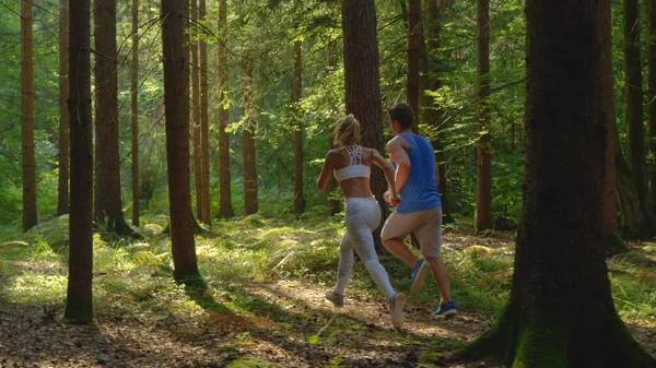 白いスポーツウェアとボーイフレンドで認識できない女性は森の中をジョギング. — ストック写真