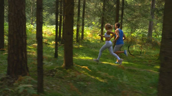 Male and female training partners running together through scenic green woods. —  Fotos de Stock