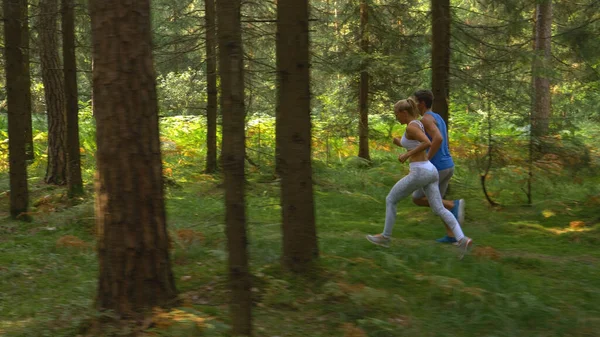 Fit young couple in brand new sportswear runs down narrow forest path in summer. —  Fotos de Stock