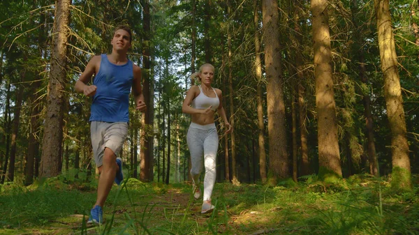 CLOSE UP: Happy woman and her boyfriend exercising by running through the woods. —  Fotos de Stock