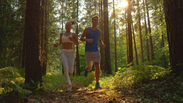 Atlétikai lány és a barátja kocognak a napsütötte erdei ösvényen.. — Stock Fotó