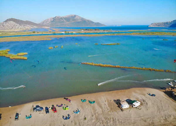 DRONE: Volando a lo largo de la playa de arena con kitesurfistas cabalgando alrededor de la bahía ventosa . — Foto de Stock