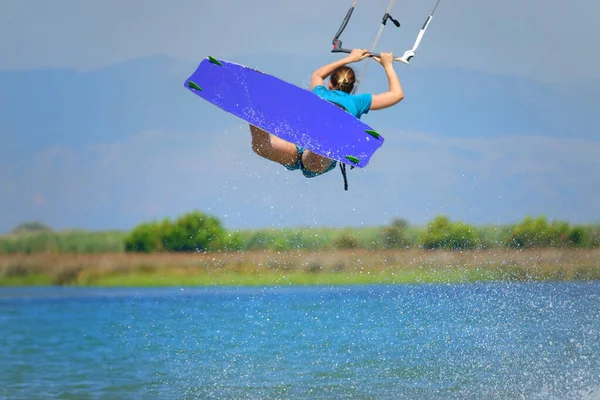Unrecognizable female kitesurfer jumps in the air and sprays the ocean water.