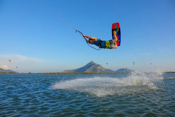 Athletic male kitesurfer jumps in the air and sprays the glassy ocean water.