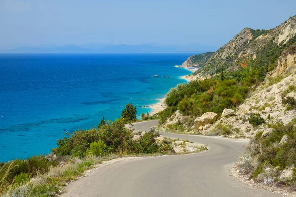 Empty asphalt road winds along rugged Mediterranean terrain and turquoise ocean. — Stock Photo, Image