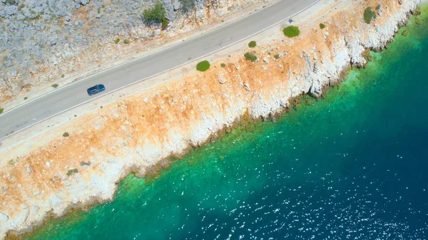 AERIAL: Flying along a tourist car cruising down empty coastal road on sunny day — Stock Photo, Image