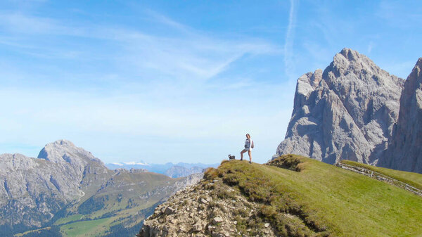 AERIAL: Woman observing the picturesque mountain landscape with her little dog.