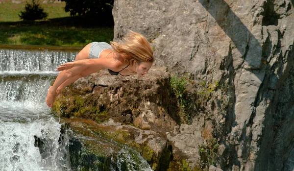 Ajuste a menina caucasiana pula cabeça primeiro em uma lagoa fora da borda de uma cachoeira. — Fotografia de Stock