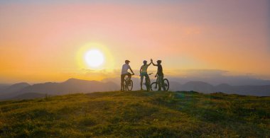 LENS FLARE: Three young cyclists riding up to edge of a hill and high fiving