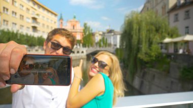 CLOSE UP: Cheerful man holds his cell phone to take a selfie with girlfriend.