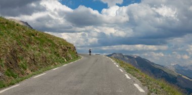 Unrecognizable road cyclist rides a bike down an mountain road on a cloudy day.