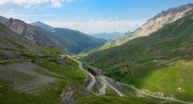 Scenic serpentine road winds up the grassy hill in the stunning French Alps.