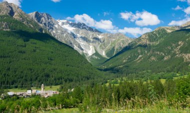 Towering mountains surround the idyllic rural town hiding behind green forest.