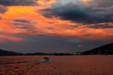 Small boat sails towards the coastal town by lake Maggiore on a sunny evening.