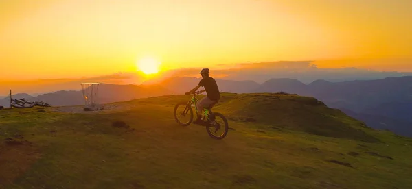 Dağ bisikletçisi resimli günbatımında çimenli bir tepede bisikletini sürüyor. — Stok fotoğraf