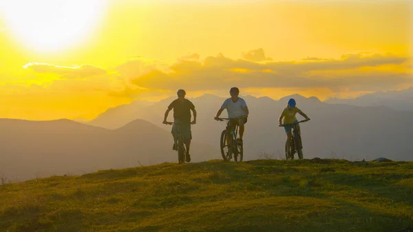 Güneşli bir akşamda üç sportif turist çayırda elektrikli bisiklet sürüyor.. — Stok fotoğraf