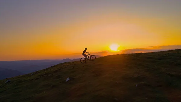 DRONE: Unrecognizable cyclist rides an electric bike uphill at golden sunset. — Stock Photo, Image