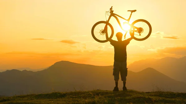 Bisiklet sürücüsü uzun bir seyahatin bitimini gün batımında kutluyor — Stok fotoğraf