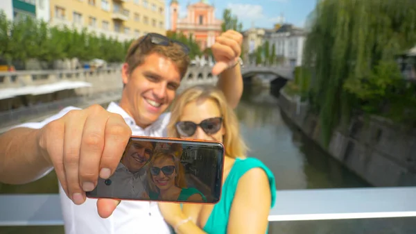 CLOSE UP Adorable tourist couple smile and wave at the phone during a skype call — Foto de Stock