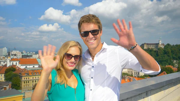 CLOSE UP: Cheerful Caucasian couple waves at camera while standing on a rooftop — Photo