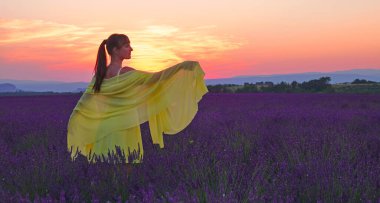 Sarı elbiseli güzel kadın, güneşli bir arifede lavanta tarlasını gözlemliyor.