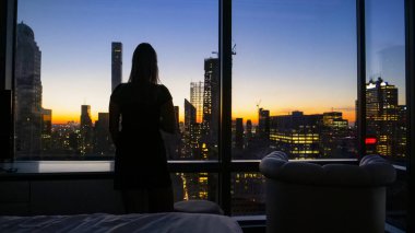 Genç bir kadın şafak vakti New York 'un altın ışıklı şehrini izliyor..