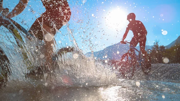 SILHOUETTE: Vänner sprutar vatten framför kameran medan de cyklar i Soca floden — Stockfoto