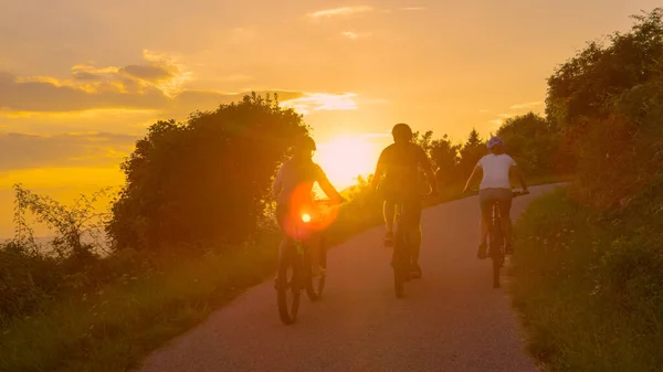 Złote wieczorne promienie słońca świecą na grupę przyjaciół jeżdżących na rowerach elektrycznych. — Zdjęcie stockowe