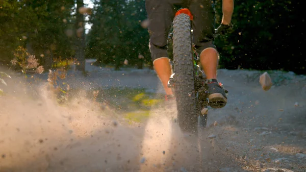 CLOSE UP: Sunbeams shine on gravel path as downhill cyclist rides past camera. — Stock Photo, Image