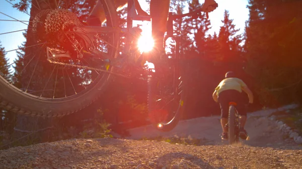 SUN FLARE: Mountain bikers ride off a ramp set in the middle of a gravel track. — Stock Photo, Image