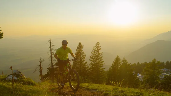 LOW ANGLE: Active male tourist pedalling an electric bike uphill at sunrise. — Stock Photo, Image