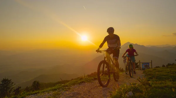 LENS FLARE: Viaggiatori felici che si godono un giro in bicicletta tra le montagne illuminate dal sole. — Foto Stock