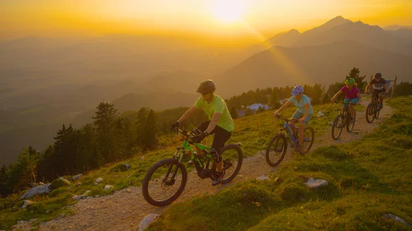 DRONE: Turisti allegri in sella a mountain bike su un sentiero panoramico al tramonto. — Foto Stock