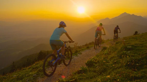 Oigenkännlig passform turister rida cyklar ner grus väg vid soluppgången. — Stockfoto