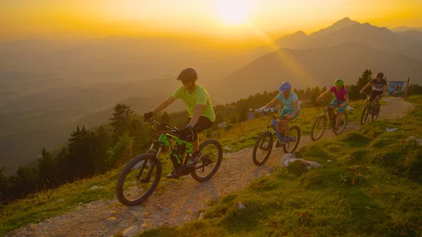 AERIAL: Gyllene kvällssolstrålar skiner på mountainbikecyklister rider upp en stig. — Stockfoto