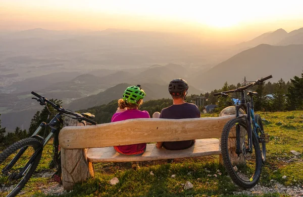 CHIUSURA: I ciclisti irriconoscibili si siedono e osservano il tramonto da una panchina — Foto Stock