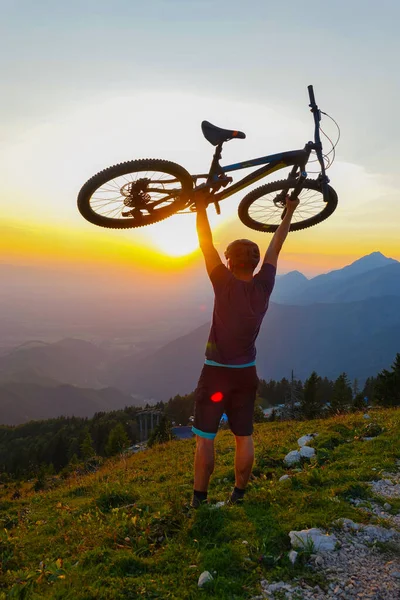 LENS FLARE: Nierozpoznawalny mężczyzna podnosi rower w powietrzu o zachodzie słońca. — Zdjęcie stockowe