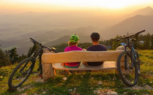 CHIUDI: Giovane uomo e donna seduti su una panchina di legno e guardare il tramonto dorato. — Foto Stock