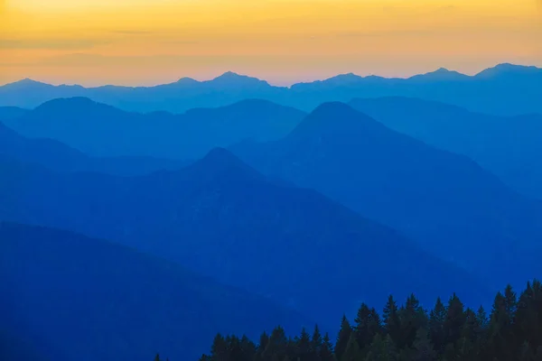 AERIAL: Vibrant yellow and blue evening sky spans above the mountain range. — ストック写真