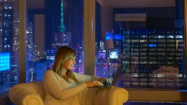CHIUDI: Donna sorridente seduta sul divano di notte e che lavora sul suo portatile. — Foto Stock