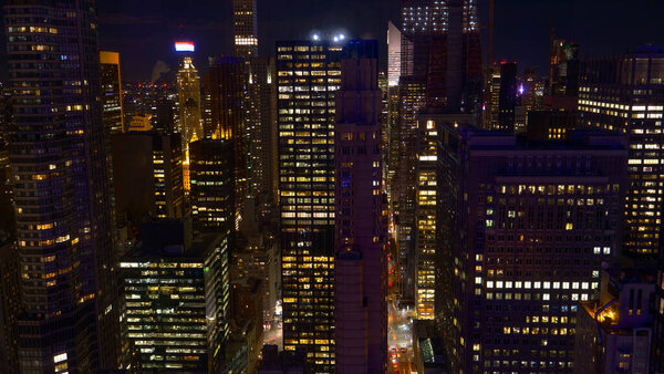 Stunning view of night time traffic moving through the buzzing streets of New York. Workers in corporate offices stay up late to extend their workday in busy metropolitan city. Bright lights of NYC