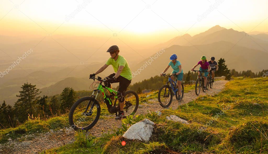 SUN FLARE Cheerful tourists ride electric bicycles up a mountain trail at sunset