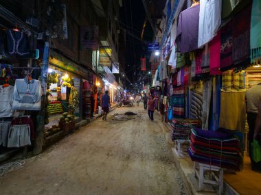Turistler Kathmandu 'da asfaltsız cadde boyunca yürürken dükkanları keşfediyorlar.