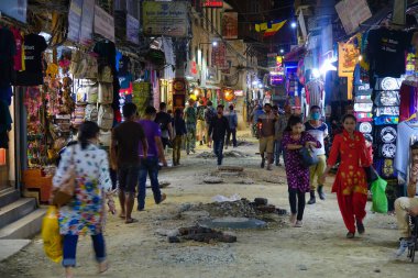 Turistik bölgede insanlar bakımsız ve asfaltsız yolda yürüyor.
