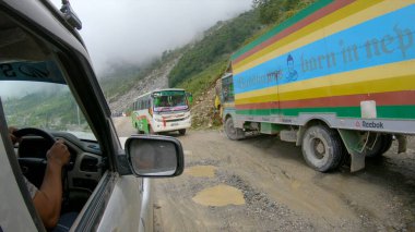 Engebeli yolun kenarına park etmiş bir turist otobüsünün ve kamyonların yanından geçmek..