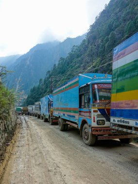 Nepal dağlarındaki çakıllı yolda renkli kamyonlar kuyruğa giriyor..