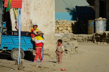 Üç yerel Tibetli çocuk kırsal bir kasabanın kirli sokaklarında oynuyorlar..